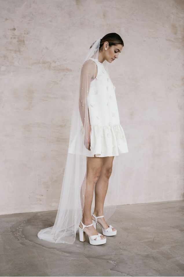 A model wearing a short shift dress that puffs out at the bottom and has daisies embroidered on it 