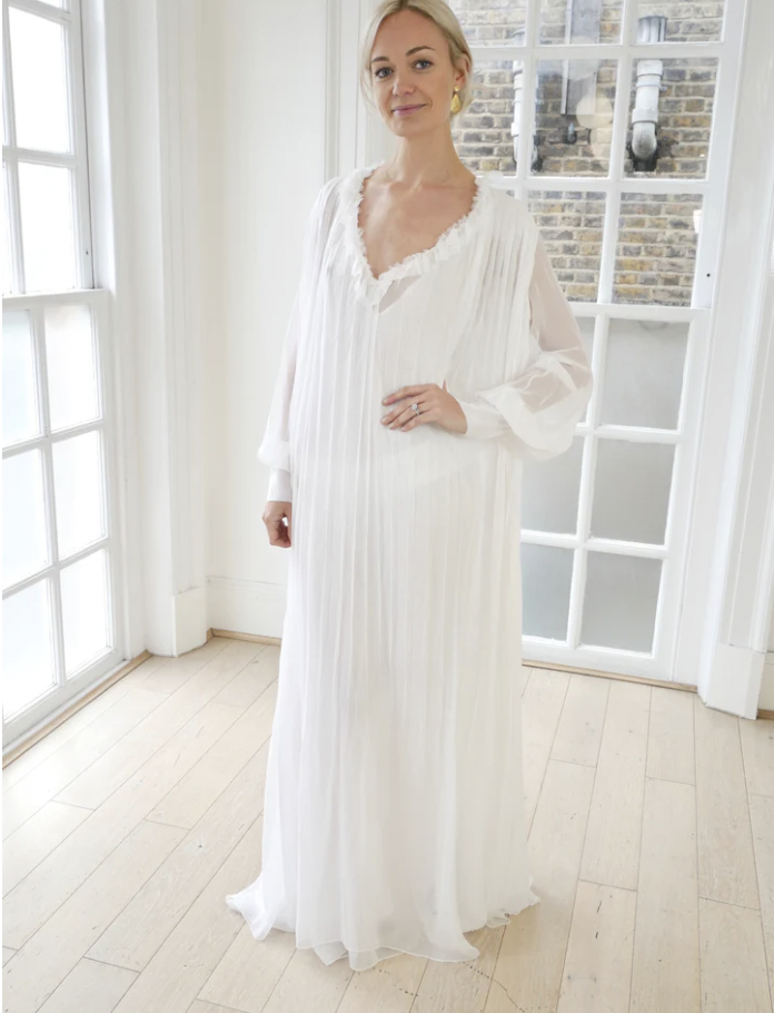 Model wearing long draped pleated dress with ruffle detail gathered at a plunging v-neck and long sleeves
