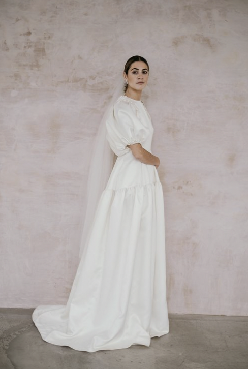 A model wearing a veil and a wedding dress with puffy sleeves and a drop waist skirt 